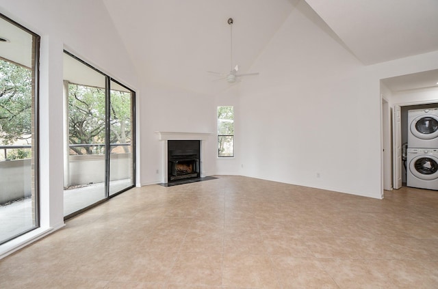 unfurnished living room featuring stacked washing maching and dryer, plenty of natural light, high vaulted ceiling, and ceiling fan