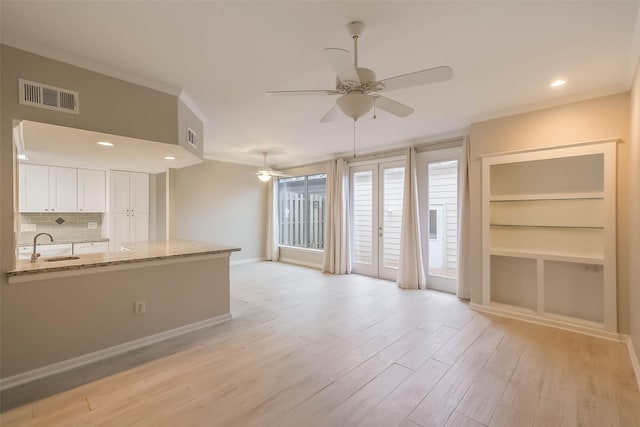 unfurnished living room with light wood finished floors, a ceiling fan, visible vents, and crown molding