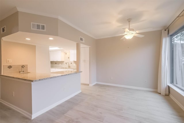 kitchen with a peninsula, visible vents, white cabinetry, light stone countertops, and tasteful backsplash