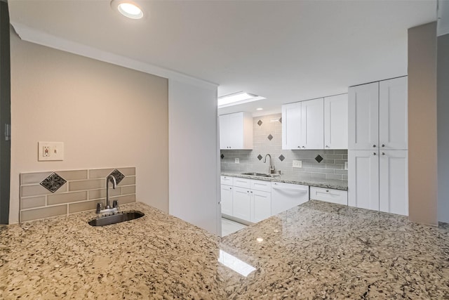 kitchen with light stone countertops, white dishwasher, white cabinetry, and a sink