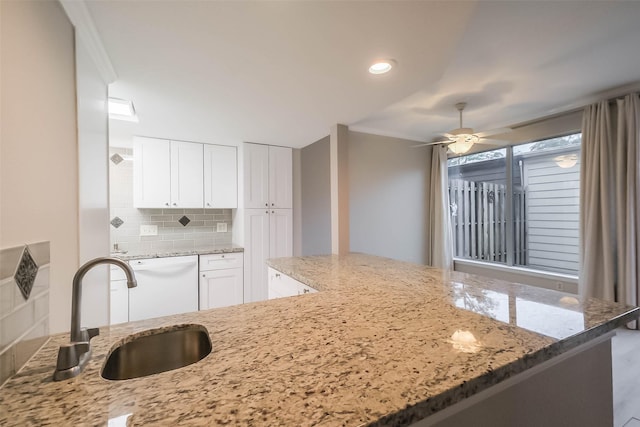 kitchen with a sink, light stone countertops, white dishwasher, white cabinetry, and backsplash