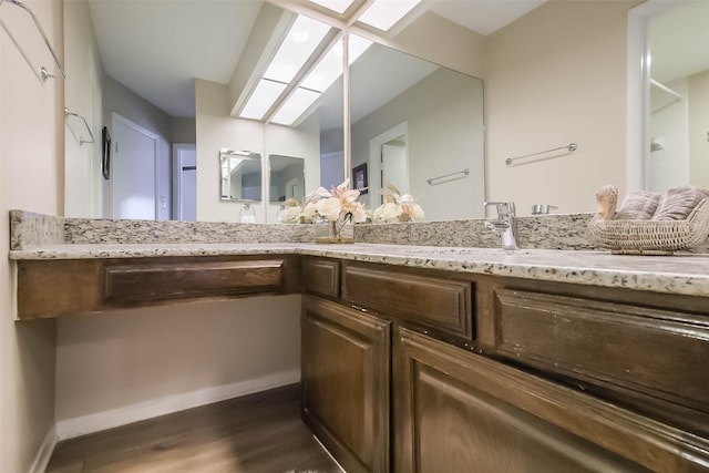 bathroom featuring a skylight, baseboards, wood finished floors, and vanity