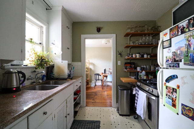 kitchen with freestanding refrigerator, light floors, white cabinetry, a sink, and gas stove