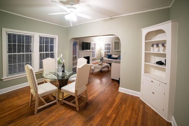 dining room with a fireplace, a ceiling fan, baseboards, ornamental molding, and dark wood finished floors