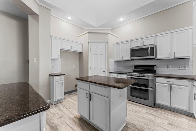 kitchen featuring appliances with stainless steel finishes, light hardwood / wood-style flooring, tasteful backsplash, white cabinets, and a kitchen island