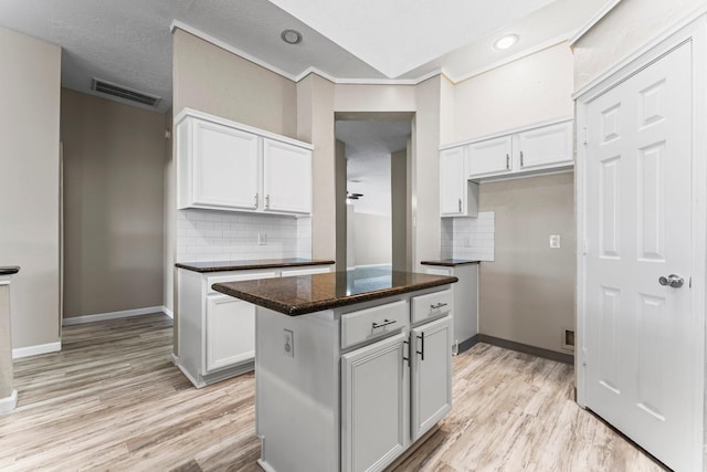 kitchen with white cabinets, a center island, backsplash, and light wood-type flooring