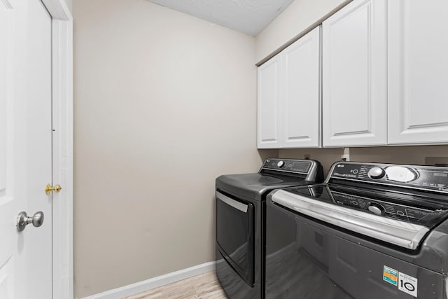 washroom with cabinets, washer and dryer, a textured ceiling, and light wood-type flooring