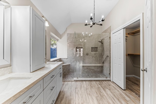 bathroom with wood-type flooring, tiled shower, lofted ceiling, vanity, and an inviting chandelier