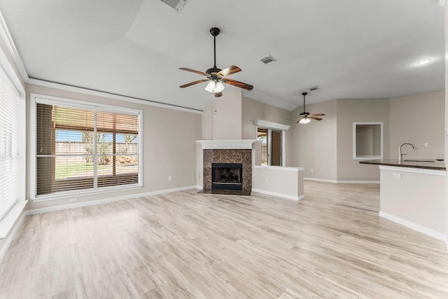 unfurnished living room featuring a fireplace, light hardwood / wood-style floors, sink, vaulted ceiling, and ceiling fan