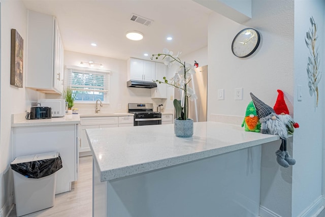 kitchen featuring stainless steel gas range oven, light stone countertops, light hardwood / wood-style floors, sink, and white cabinetry