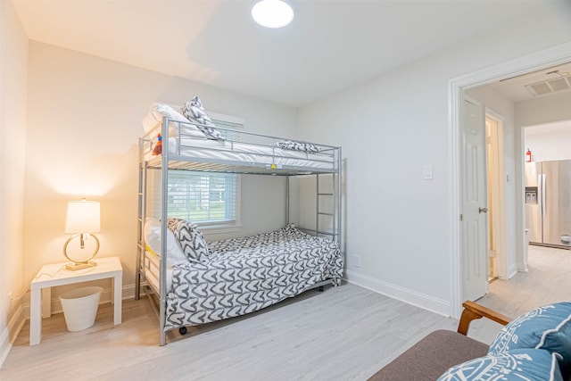 bedroom with hardwood / wood-style floors and stainless steel refrigerator with ice dispenser