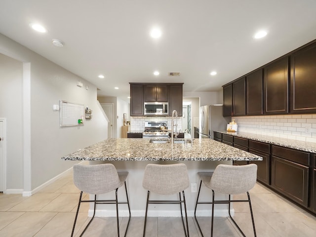 kitchen featuring appliances with stainless steel finishes, sink, a kitchen island with sink, and light stone countertops