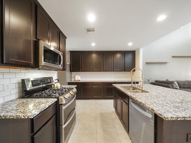 kitchen with a center island with sink, appliances with stainless steel finishes, sink, light tile patterned floors, and decorative backsplash