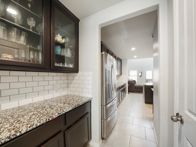 kitchen featuring decorative backsplash, stainless steel fridge, light stone counters, and dark brown cabinetry