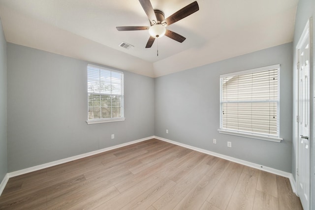 spare room featuring light wood-style floors, baseboards, visible vents, and vaulted ceiling