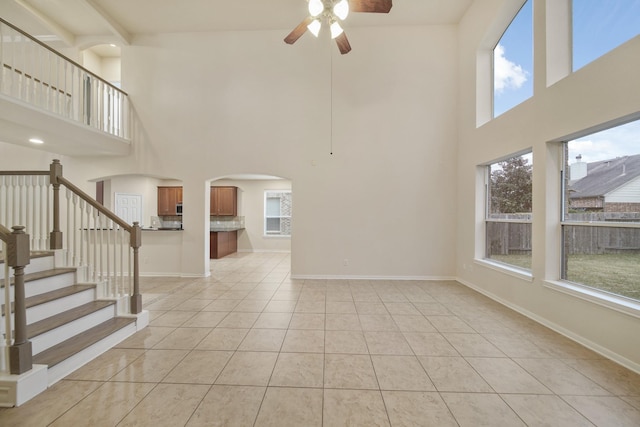 unfurnished living room with light tile patterned floors, baseboards, arched walkways, ceiling fan, and stairs