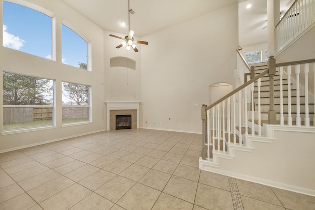 unfurnished living room featuring stairway, a tiled fireplace, light tile patterned flooring, ceiling fan, and baseboards