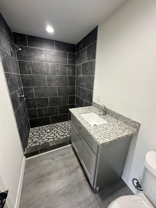 bathroom featuring hardwood / wood-style flooring, toilet, vanity, and tiled shower