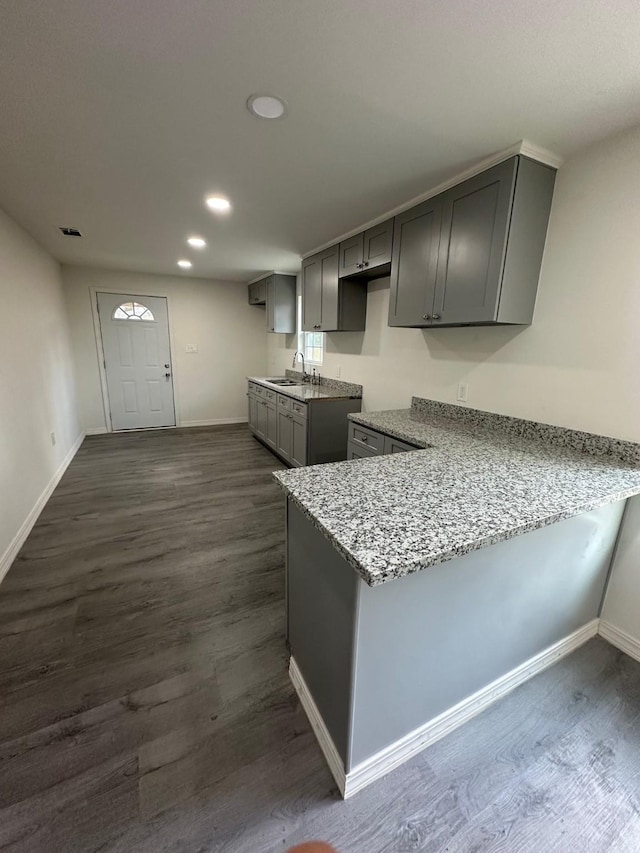 kitchen with sink, light stone counters, gray cabinetry, and dark hardwood / wood-style floors