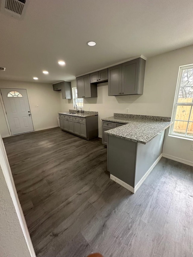 kitchen with kitchen peninsula, gray cabinetry, sink, light stone counters, and dark hardwood / wood-style floors