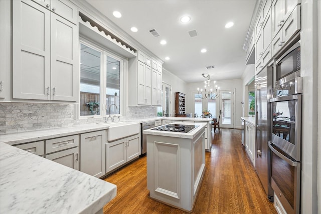 kitchen featuring a center island, decorative light fixtures, light stone counters, appliances with stainless steel finishes, and crown molding