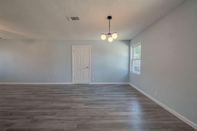 unfurnished room with a textured ceiling, dark hardwood / wood-style floors, and an inviting chandelier