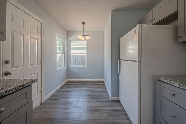 kitchen with hanging light fixtures, white refrigerator, light stone counters, and gray cabinetry