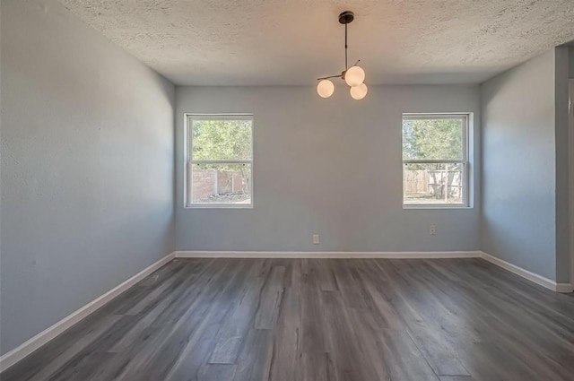 empty room featuring a textured ceiling, dark wood-type flooring, and a chandelier