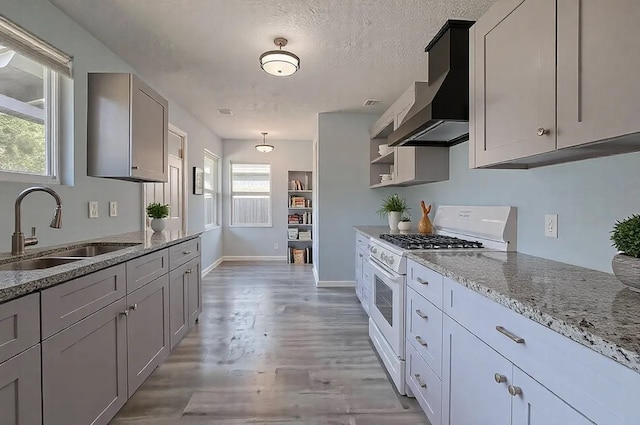 kitchen with wall chimney exhaust hood, a textured ceiling, gray cabinets, sink, and white gas range oven