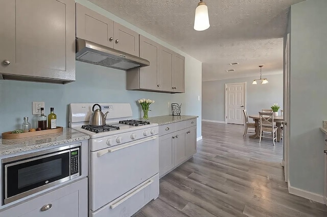 kitchen with hanging light fixtures, white gas range oven, stainless steel microwave, and light hardwood / wood-style flooring