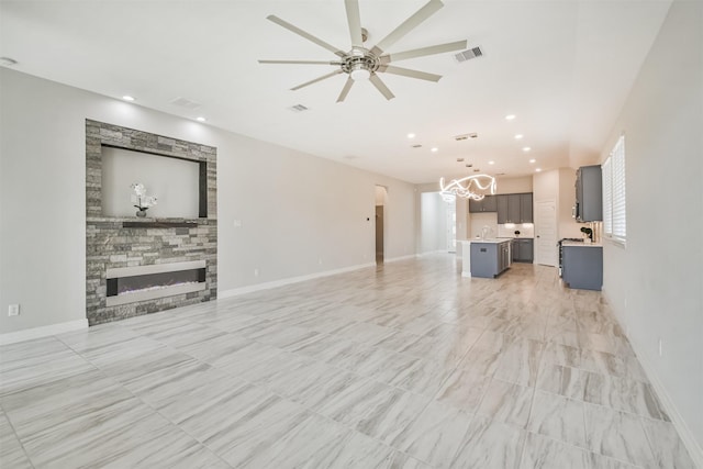 living room with a stone fireplace and ceiling fan with notable chandelier