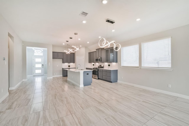 kitchen with an island with sink, hanging light fixtures, stainless steel appliances, sink, and decorative backsplash