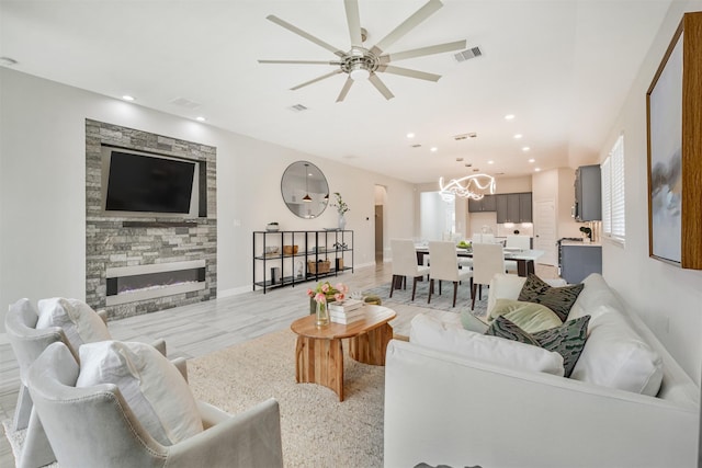 living room with ceiling fan with notable chandelier and a stone fireplace