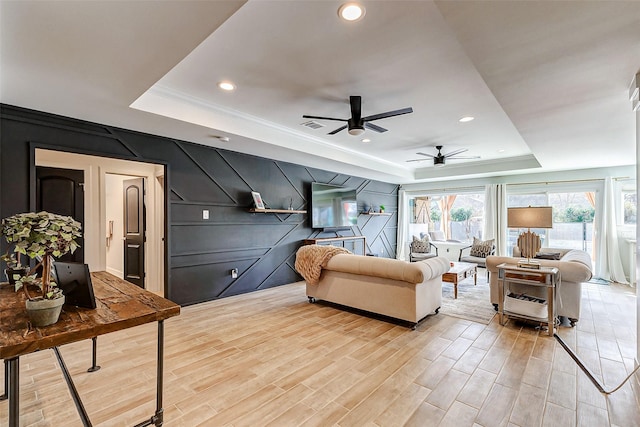 living room featuring light wood-style floors, a tray ceiling, a decorative wall, and recessed lighting