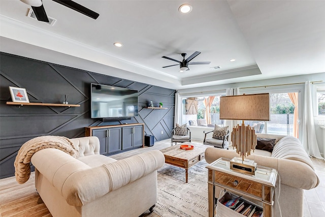 living room with ceiling fan, visible vents, a tray ceiling, and ornamental molding