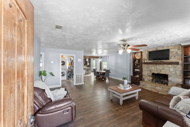 living room featuring a stone fireplace, a textured ceiling, dark wood-type flooring, stacked washing maching and dryer, and built in features