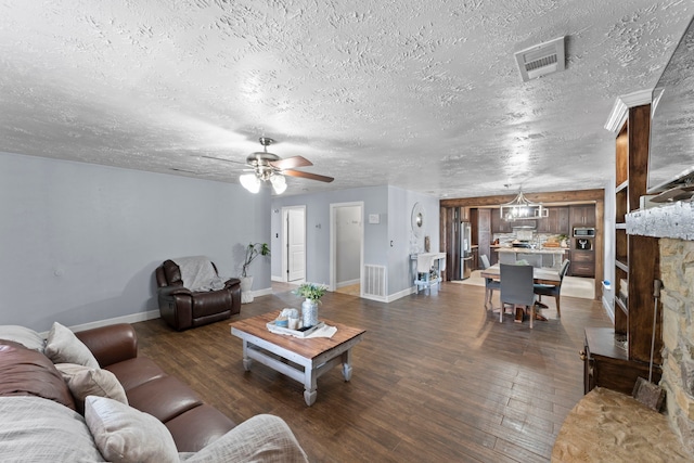 living room featuring a textured ceiling, a stone fireplace, dark hardwood / wood-style floors, and ceiling fan