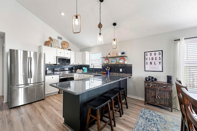 kitchen with stainless steel appliances, pendant lighting, a breakfast bar, white cabinetry, and dark stone countertops