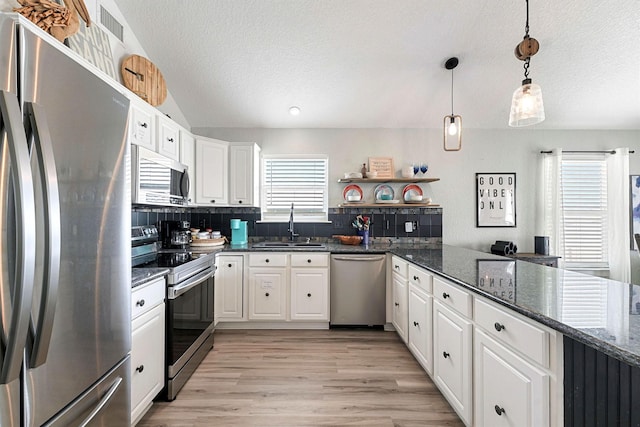 kitchen with sink, dark stone counters, decorative light fixtures, stainless steel appliances, and white cabinets