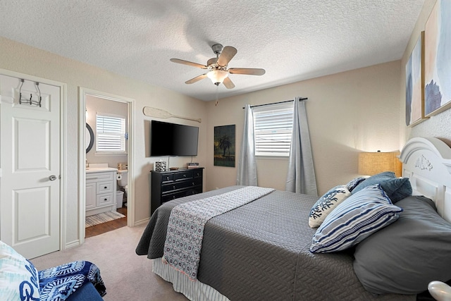 bedroom with a textured ceiling, light carpet, ensuite bathroom, and ceiling fan