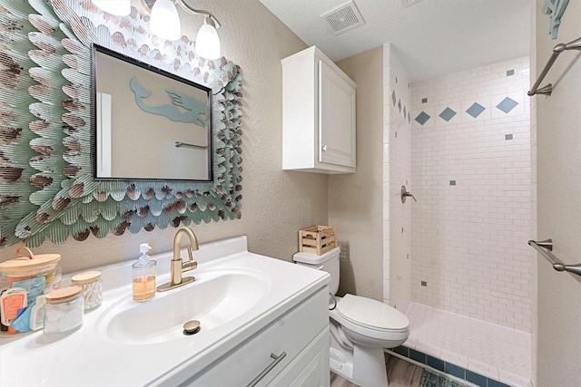 bathroom with a textured ceiling, toilet, vanity, and tiled shower