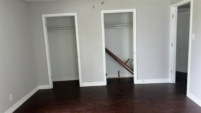 unfurnished bedroom featuring baseboards, dark wood-style flooring, and two closets