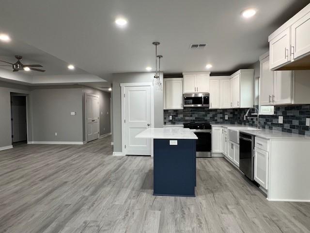 kitchen featuring hanging light fixtures, stainless steel appliances, white cabinets, ceiling fan, and a kitchen island