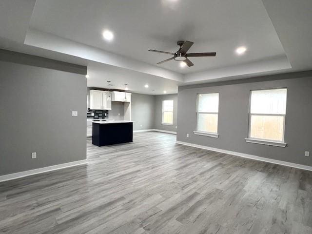 unfurnished living room featuring a tray ceiling, ceiling fan, and hardwood / wood-style floors