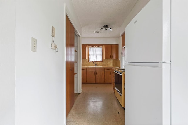 kitchen featuring electric range, white refrigerator, sink, a textured ceiling, and decorative backsplash