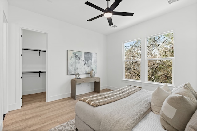 bedroom with ceiling fan, a walk in closet, and light hardwood / wood-style flooring