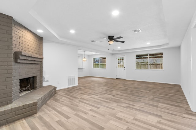 unfurnished living room with ceiling fan, light wood-type flooring, a raised ceiling, and a brick fireplace