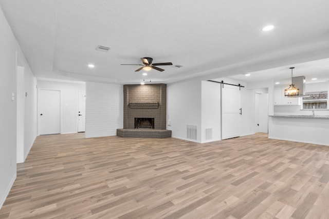 unfurnished living room featuring light hardwood / wood-style flooring, a textured ceiling, ceiling fan, a barn door, and a brick fireplace