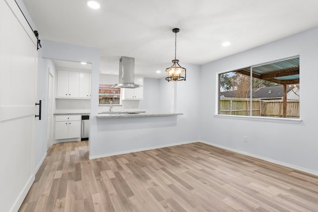 kitchen featuring island range hood, white cabinetry, a barn door, kitchen peninsula, and hanging light fixtures