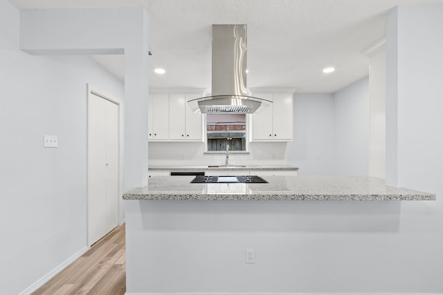 kitchen with island range hood, white cabinets, kitchen peninsula, and light stone counters